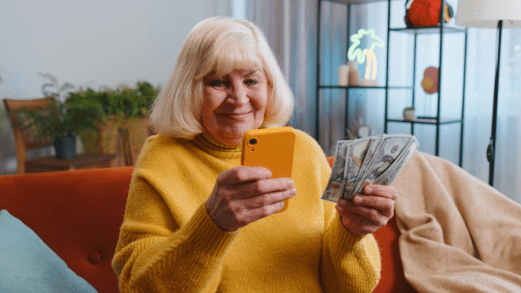 A person sitting on a couch holding money and looking at their phone